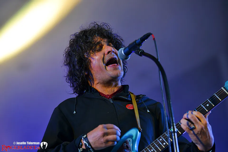 Sångare med lockigt hår och gitarr sjunger i mikrofonen